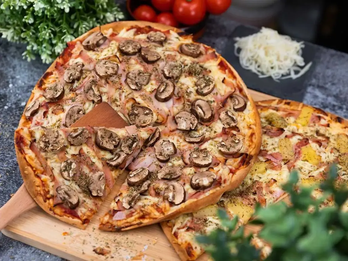 En härlig liba pizza med champinjoner och skinka, redo att avnjutas. Bredvid ligger en annan pizza med ananas och skinka.