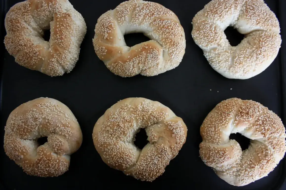 Sex gyllene simit, täckta med sesamfrön, ligger på en svart plåt. Perfekt för ett simit recept!