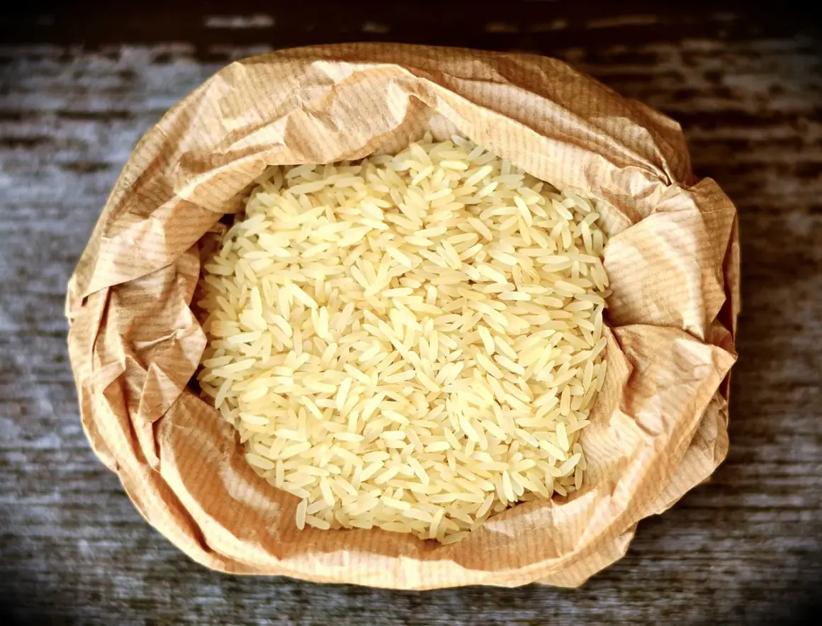 En påse med basmati eller jasminris ligger på en träyta. Riset är ljust och kornen är långa och smala.