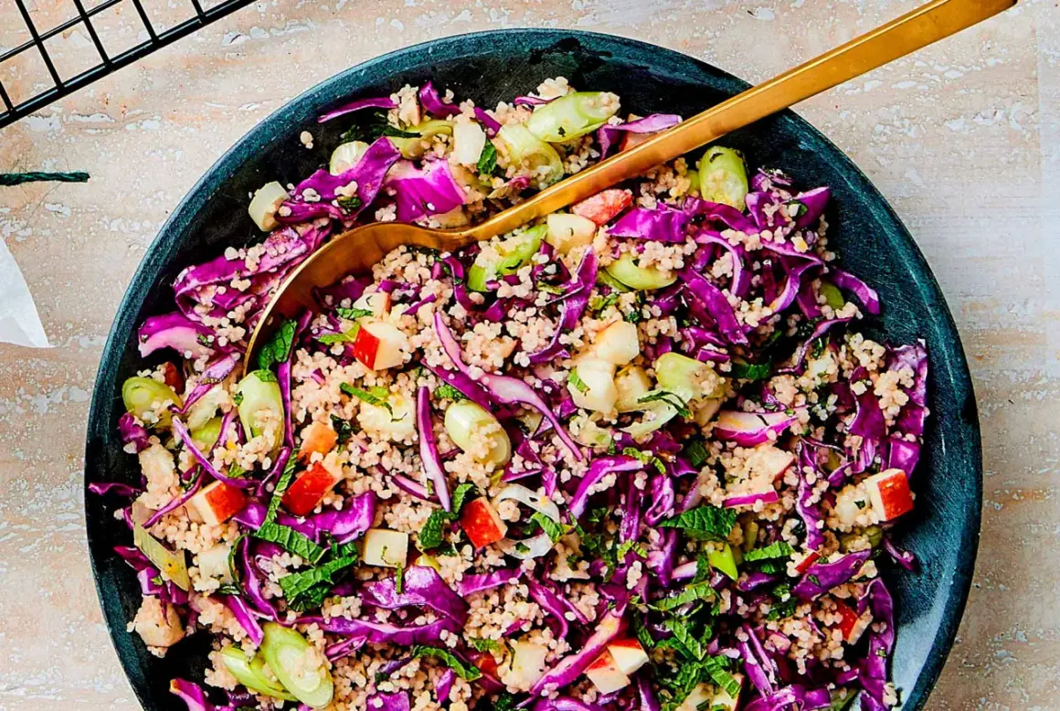 En färgstark couscous sallad med rödkål, äpple och färska örter. En gyllene sked vilar i den fräscha rätten.