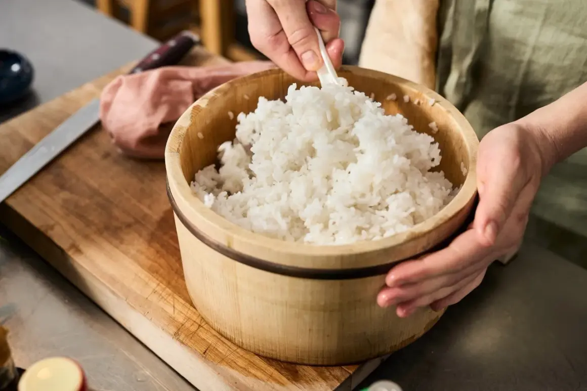 En person blandar nykokt ris i en träskål. En påminnelse om var kommer ris ifrån och hur det förbereds för sushi.