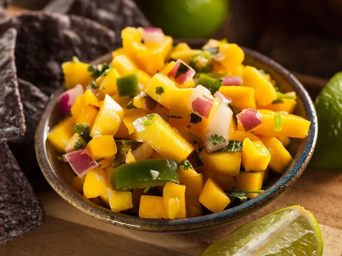 En skål med färgglad mango sallad, med tärnad mango, rödlök, grön paprika och koriander. Serveras med tortillachips och lime.