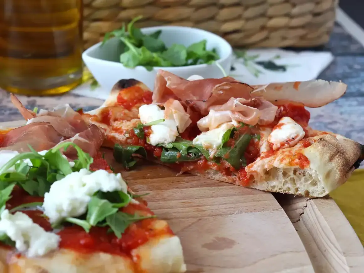 En skiva pinsa med prosciutto, mozzarella och ruccola. En härlig pinsa topping som ser utsökt ut.