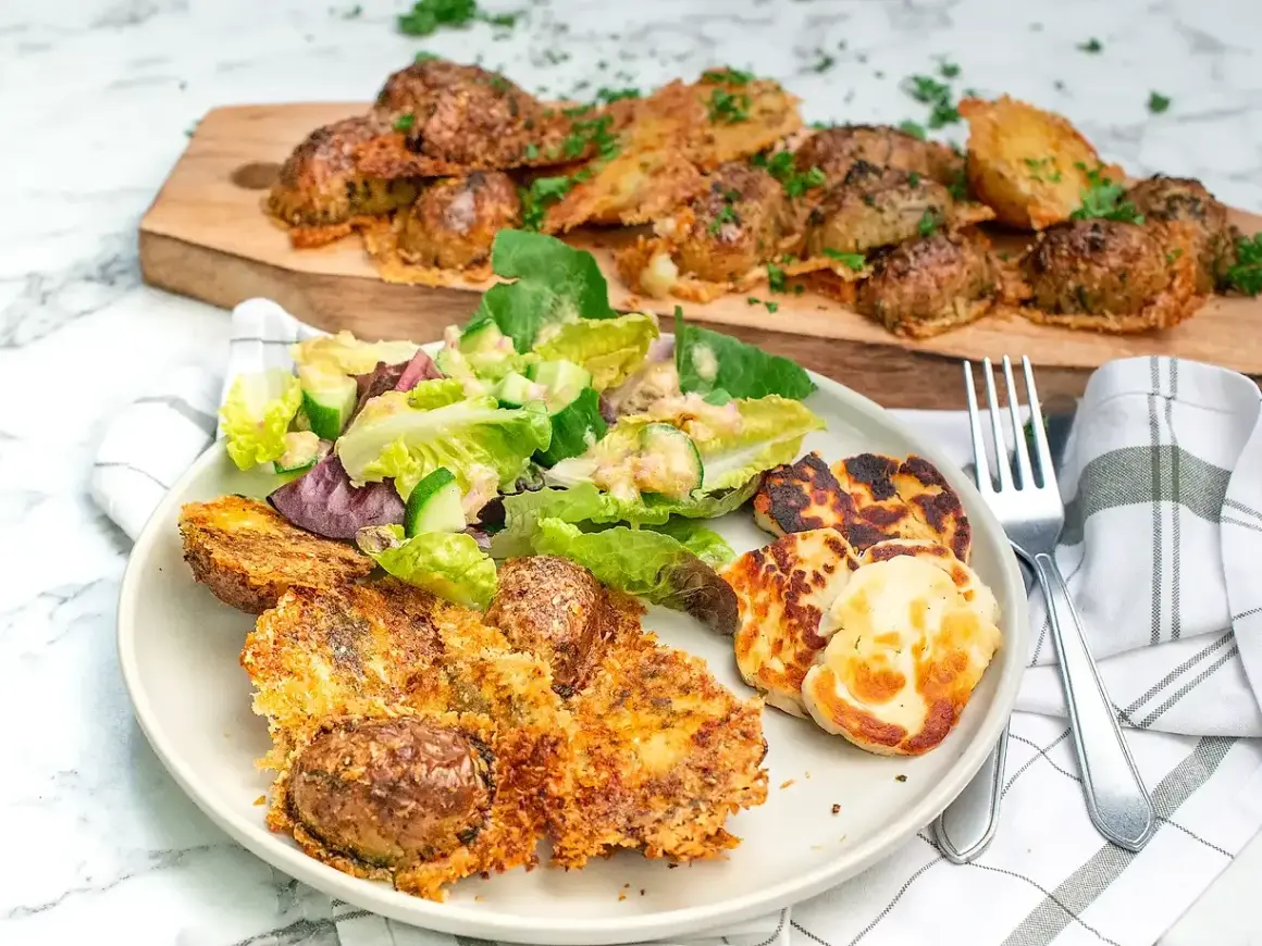 Krispiga, ugnsbakade potatisar med ostpanering serveras med en fräsch sallad och grillad halloumi. En härlig måltid!