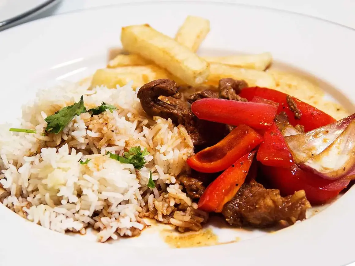 En tallrik med lomo saltado: ris, pommes frites, strimlat nötkött, rödlök och röd paprika.