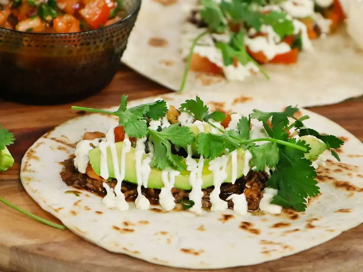 En närbild på en taco med köttfärs, avokado, koriander och en vit sås. Perfekt för ett tacokrydda recept!