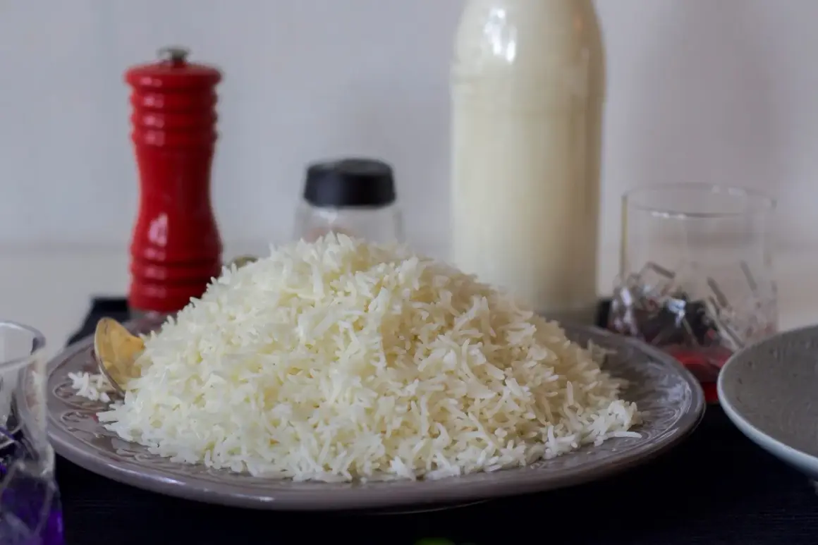 En hög med fluffigt, nykokt långkornigt ris på en tallrik. Bredvid står en röd pepparkvarn och en flaska mjölk.