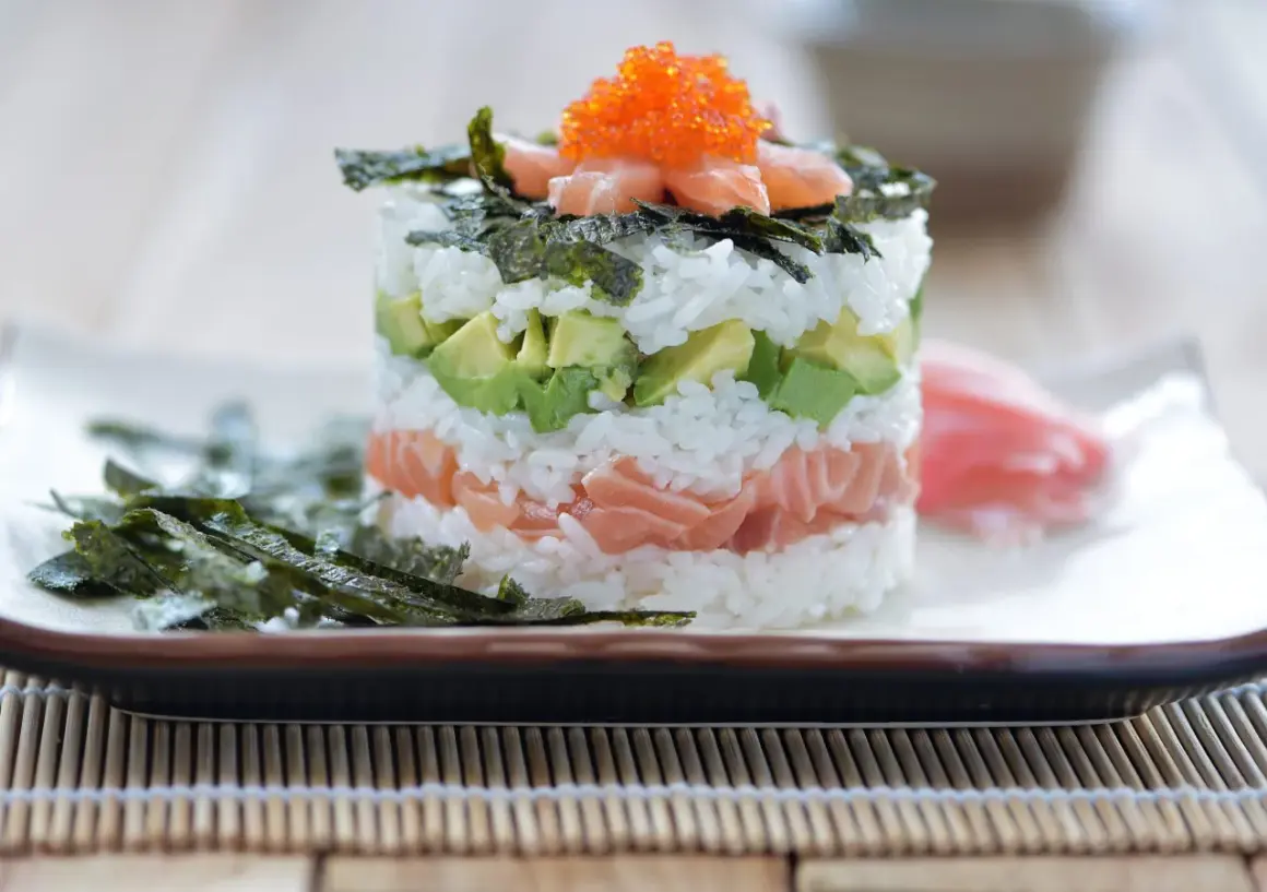 En vacker sushi tårta med lax, avokado och ris, toppad med rom och nori. En festlig rätt för alla sushiälskare.