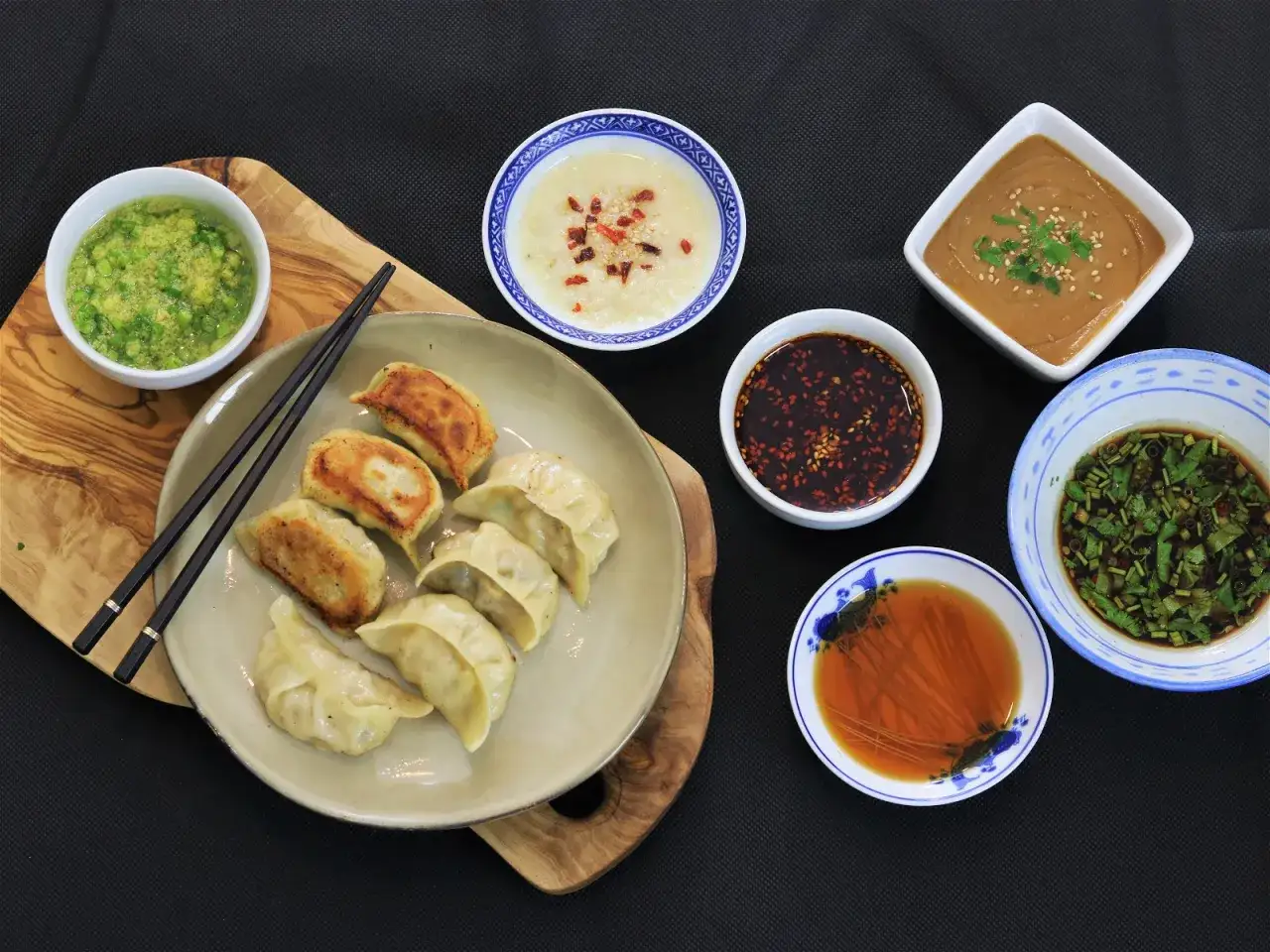 En tallrik med dumplings och flera skålar med olika dumpling sås, inklusive en grön, en mörk och en ljusare variant.