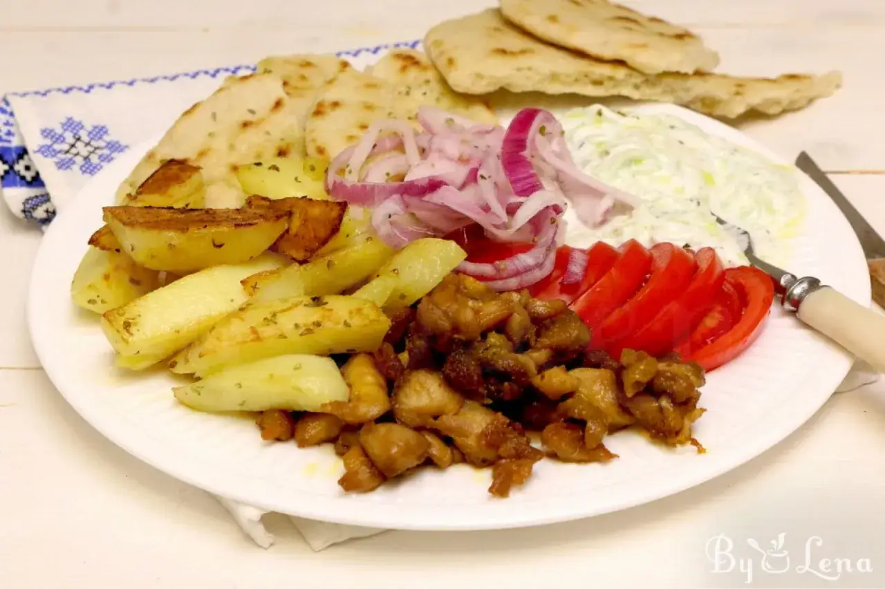 En tallrik med kyckling gyros, pommes frites, pitabröd, tomater, rödlök och tzatziki.