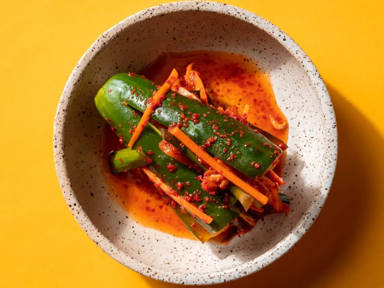 En skål med kimchi gurka, kryddig och färgglad, med strimlad morot och vitlök.
