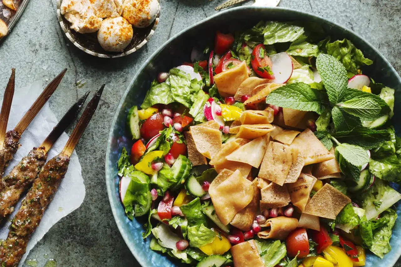En stor, blå skål fylld med en färgglad fattoush sallad med krispiga pitabrödskrutonger, grönsaker och granatäppelkärnor.