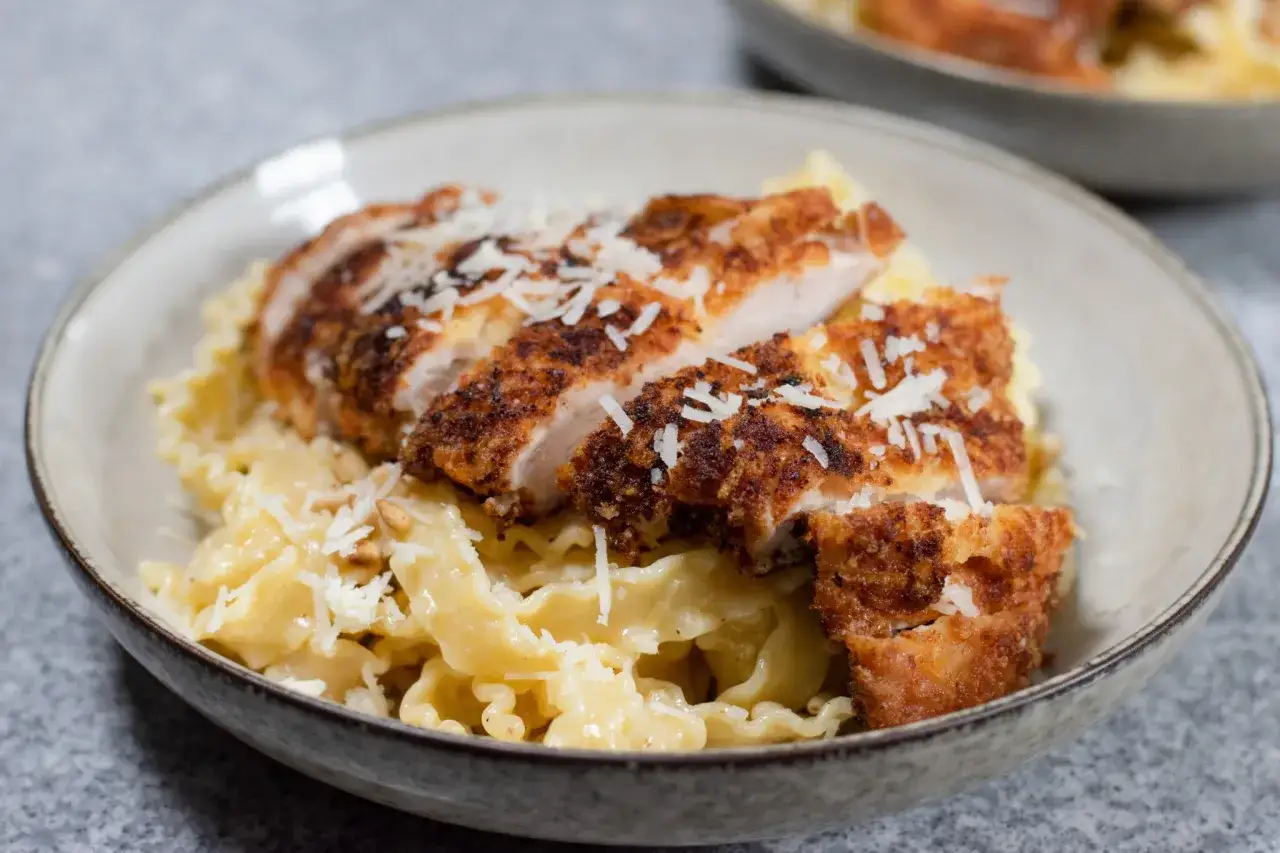 Krispig panko kyckling skuren i skivor, serverad på krusig pasta med riven parmesanost.