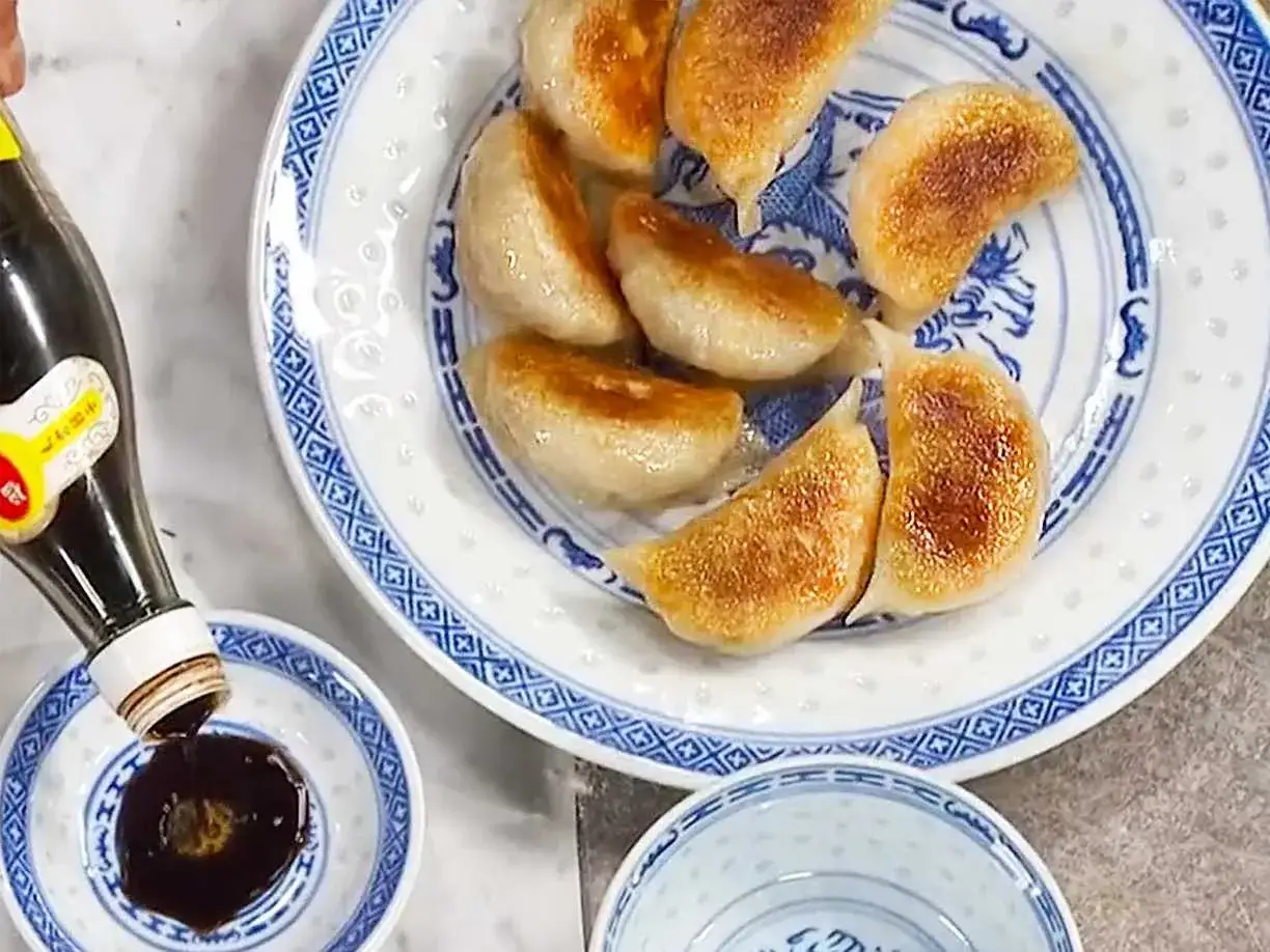 Stekta vegetariska dumplings serveras på en blåvit tallrik. Sojasås hälls upp i en liten skål. Ett perfekt vegetariskt dumplings recept!