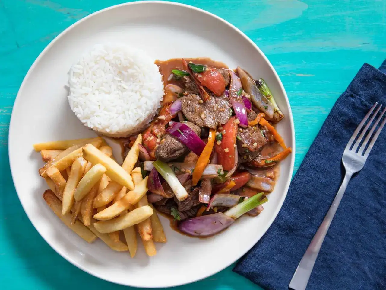 En tallrik med lomo saltado, ris och pommes frites. Rätten innehåller strimlat nötkött, lök, tomat och chili.