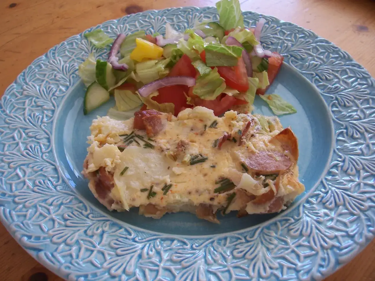 En bit omelett i ugn med bacon och gräslök, serverad med en fräsch sallad på en vacker blå tallrik.
