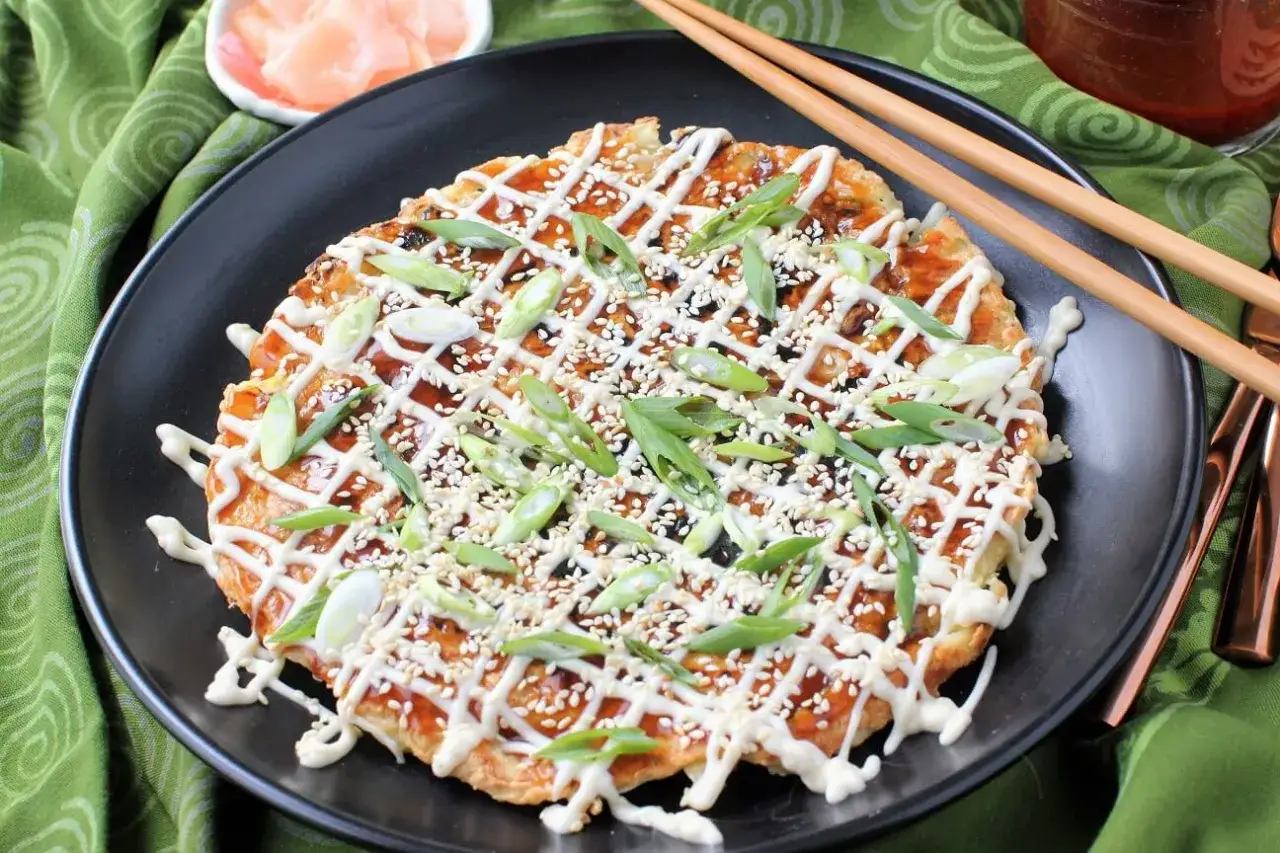 En läcker japansk kålpannkaka toppad med majonnäs, sesamfrön och salladslök. Serveras med ätpinnar och inlagd ingefära.