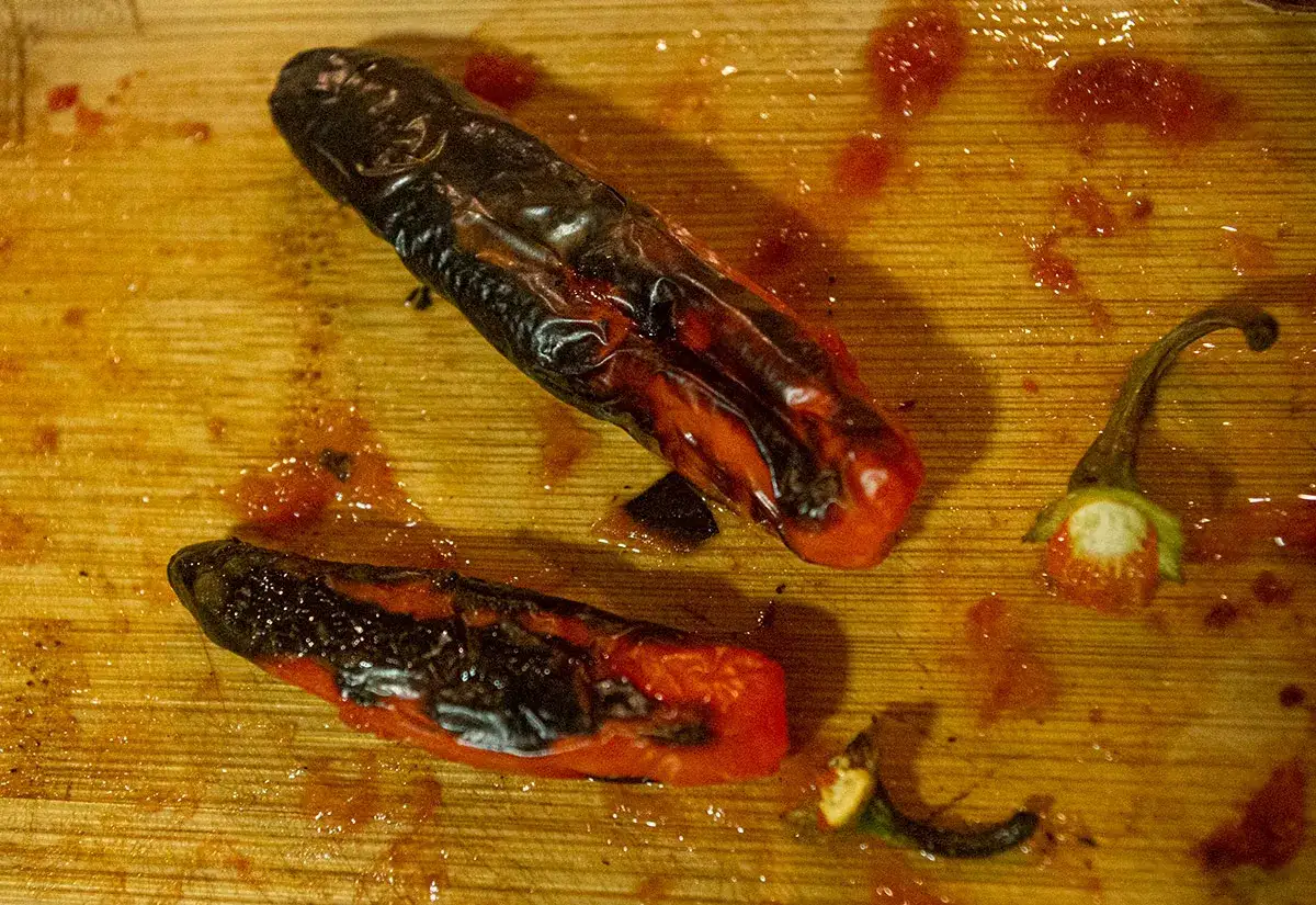 Två rostade chilis, en hel och en delad, ligger på en träskärbräda med chilisås.
