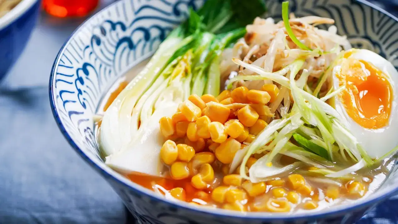 En skål med väldoftande ramen soppa med majs, böngroddar, pak choi och ett perfekt kokt ägg.