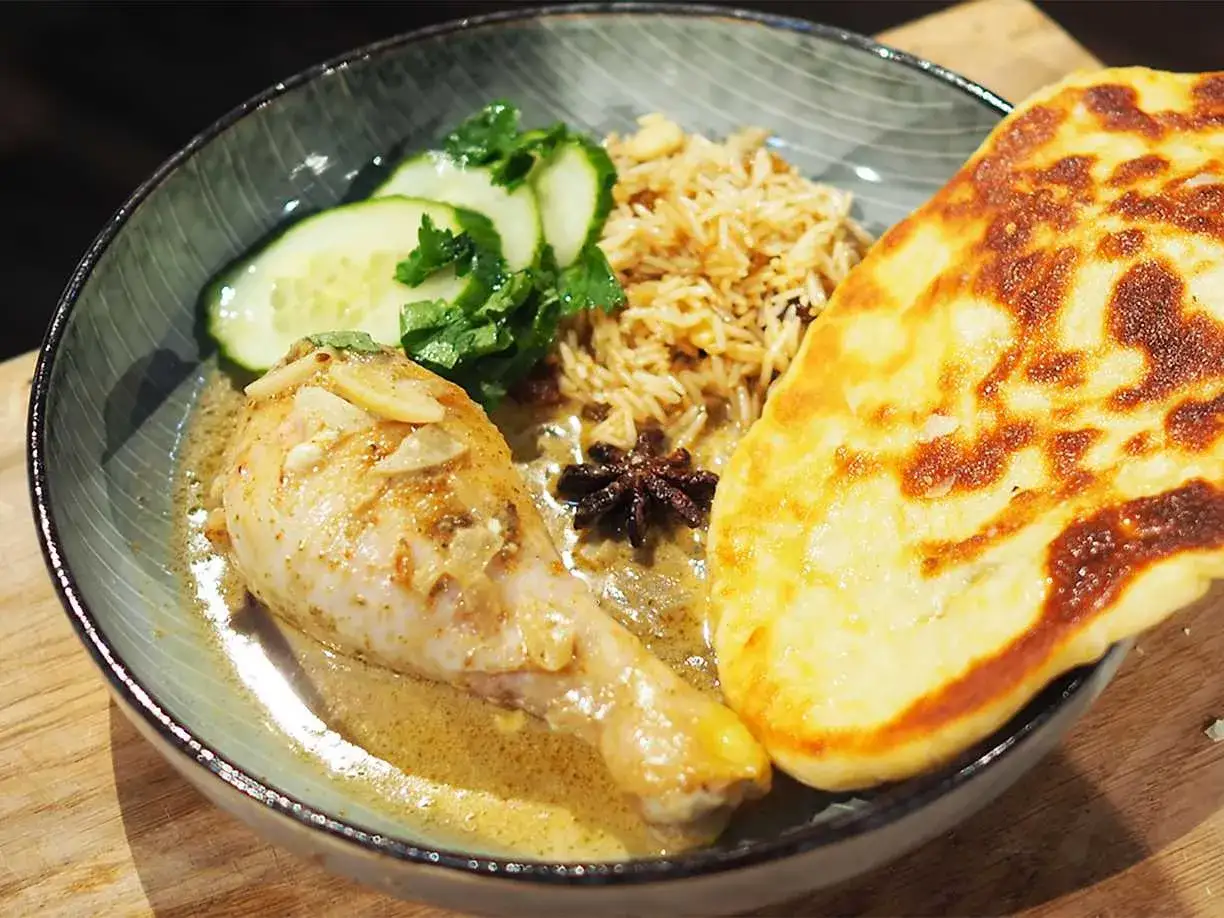 En läcker kycklingklubba i krämig sås, serverad med ris, gurka och naanbröd. En härlig butter chicken-upplevelse.