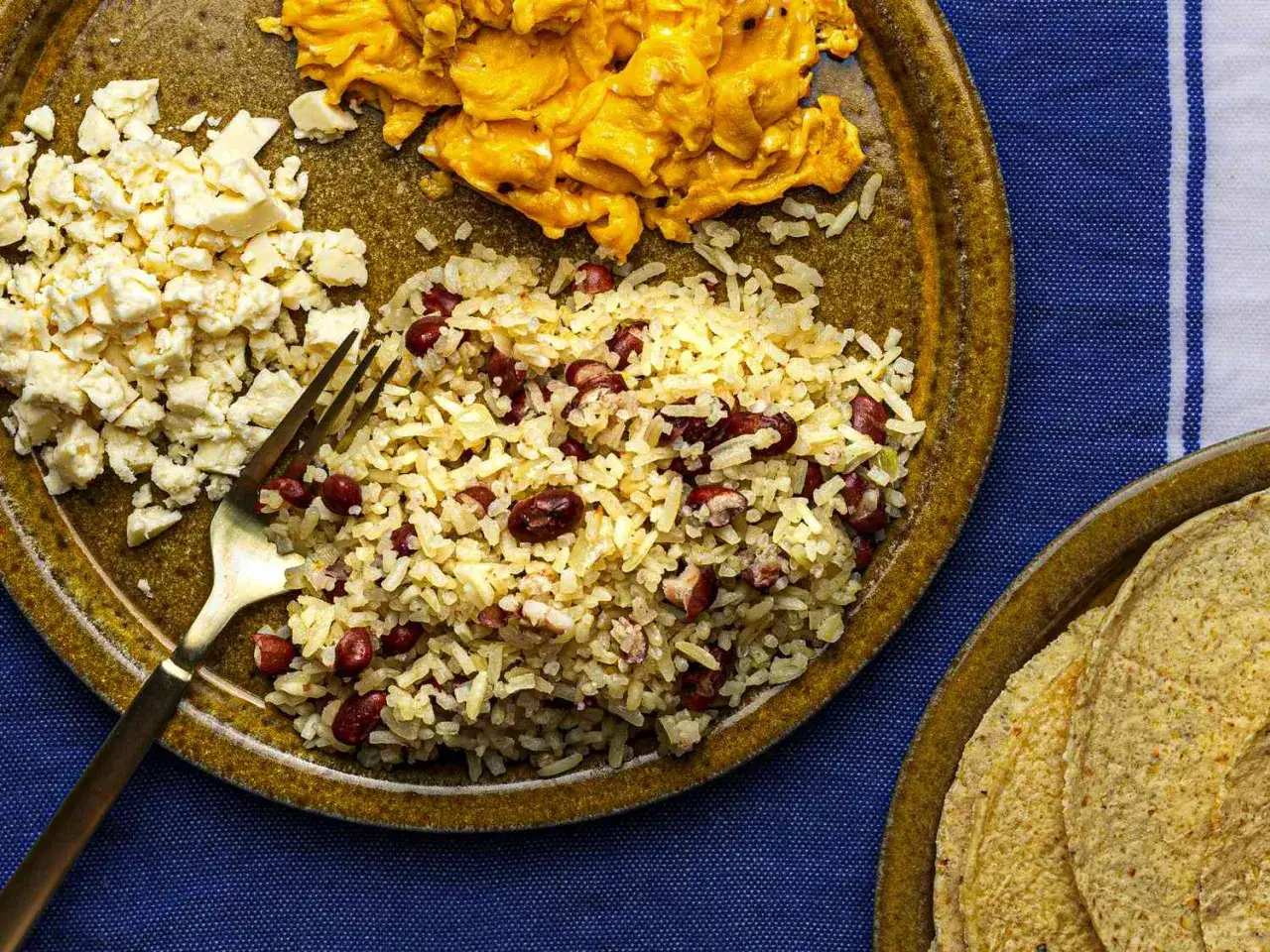 En tallrik med gallo pinto, &auml;ggr&ouml;ra och ost. En gaffel ligger i riset. Tortillas syns p&aring; en annan tallrik.