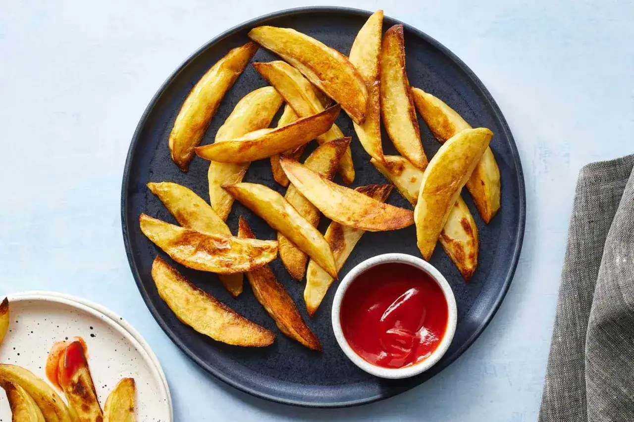 En tallrik med gyllene klyftpotatis i ugn, redo att doppas i ketchup. Perfekt som tillbehör eller eget snacks.