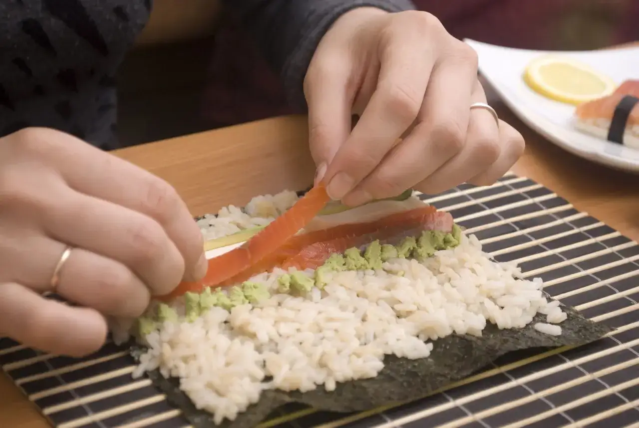 H&auml;nder l&auml;gger lax p&aring; ris och wasabi f&ouml;r att rulla sushi maki.