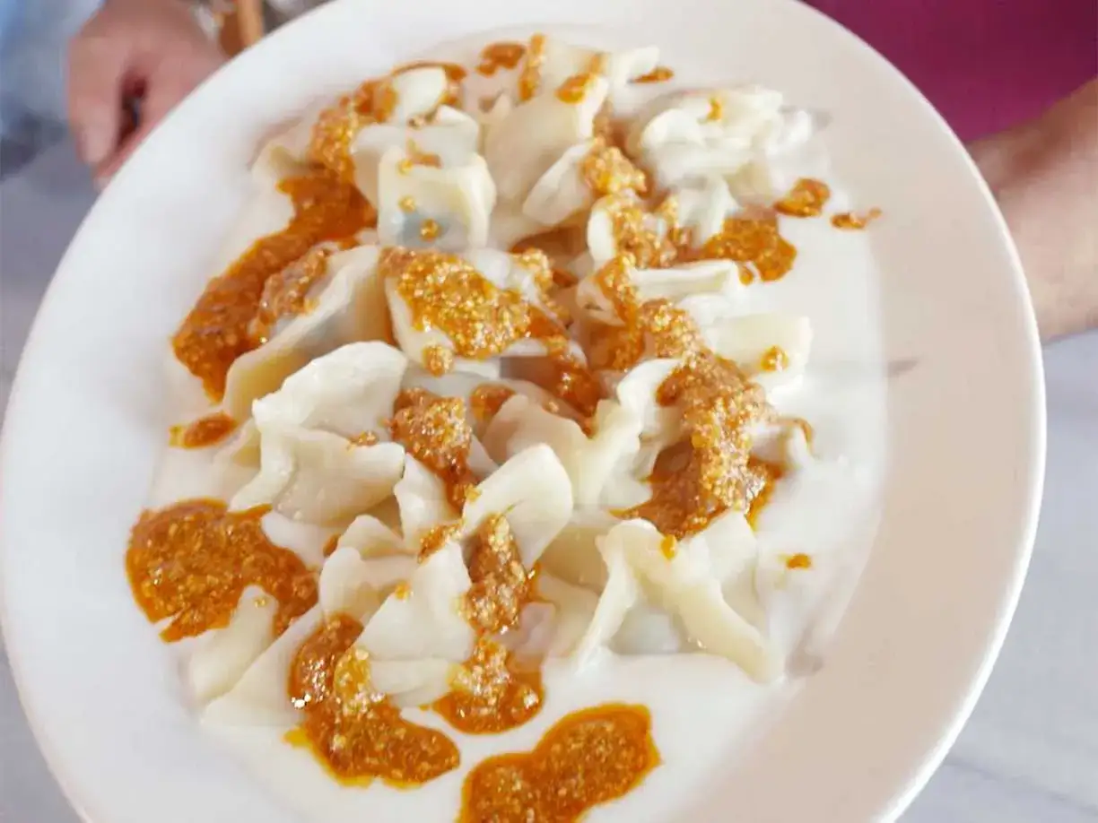 En tallrik med manti, små dumplings i en krämig sås med en kryddig topping. Ett utsökt manti recept!