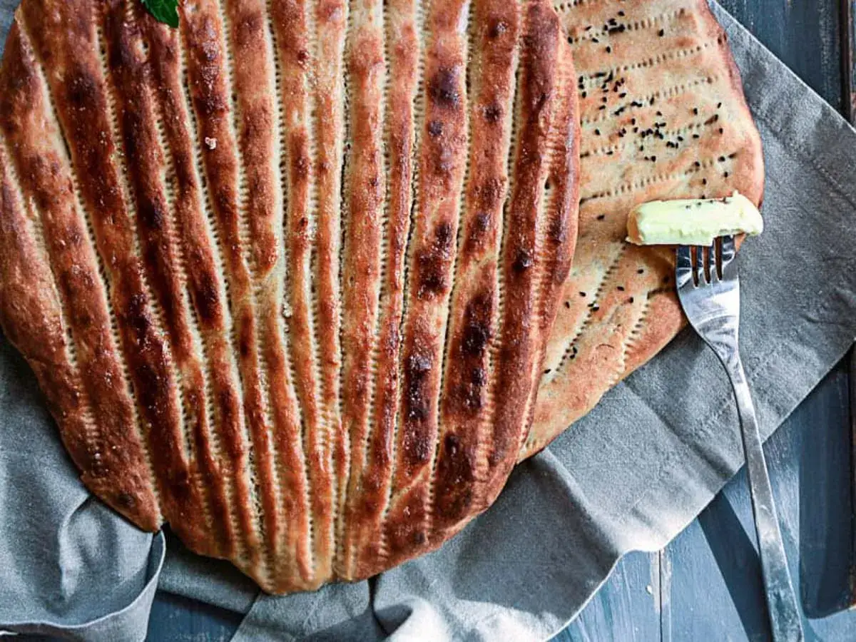 Två gyllenbruna, randiga bröd, perfekt för ett bolani recept. En gaffel med smör ligger på det ena brödet.