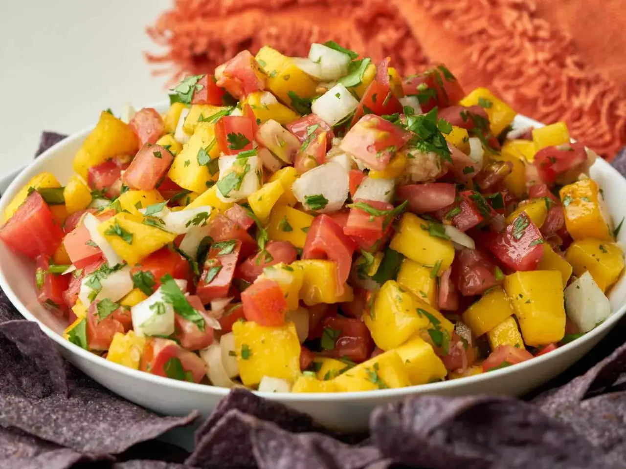 En skål med färgglad mangosalsa, perfekt för ett somrigt mangosalsa recept. Tomater, lök och koriander blandas med saftiga mangobitar.