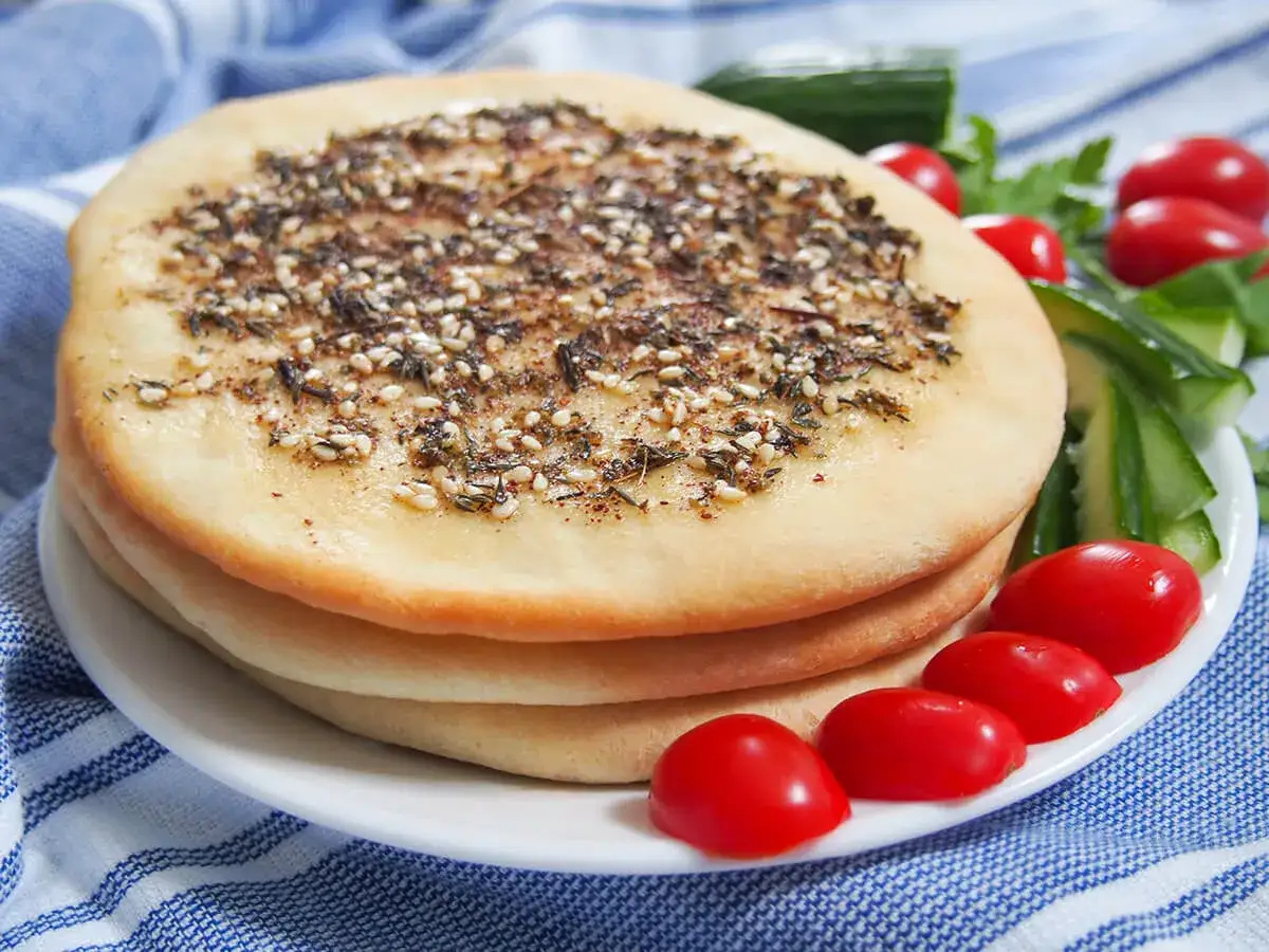 En stapel manakish med za'atar och sesamfrön, serverad med körsbärstomater och gurka. Ett enkelt manakish recept.