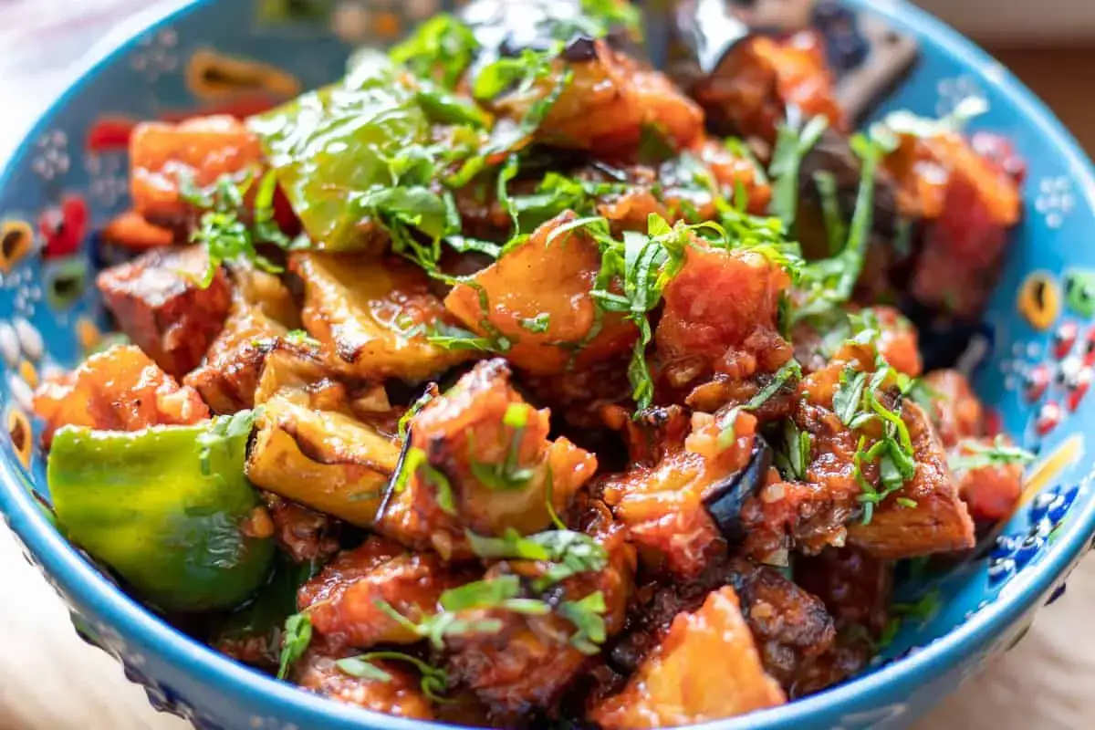 En skål med mustig imam bayildi, en klassisk auberginerätt med tomater och paprika, toppad med färska örter.