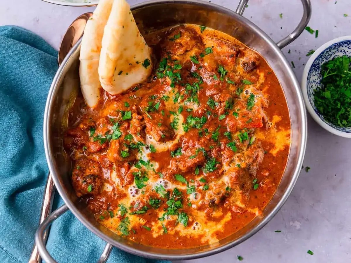 En krämig tikka masala med kycklingbitar, toppad med färsk koriander och serverad med naanbröd.