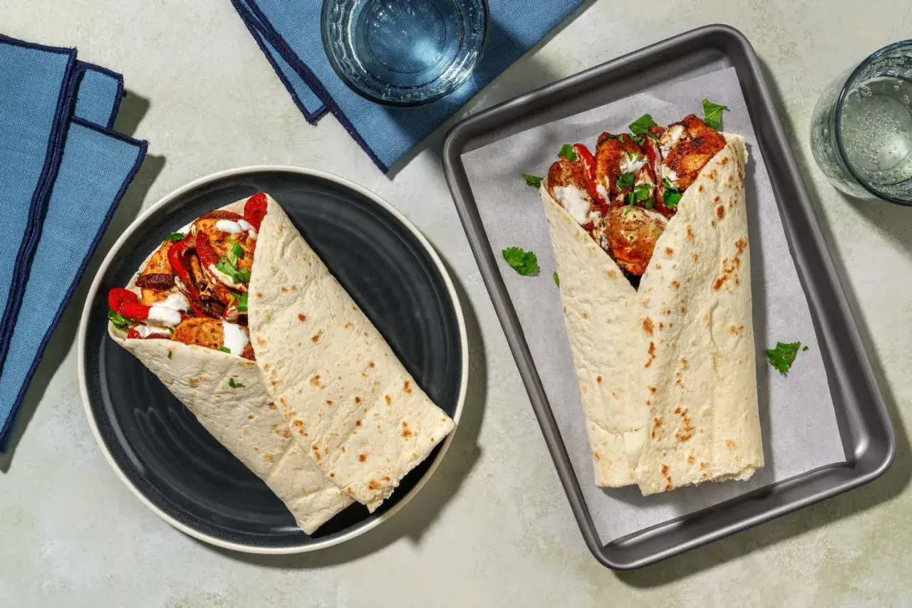 Två saftiga chicken burritos med kyckling, paprika och sås. En ligger på en tallrik, den andra på en plåt.