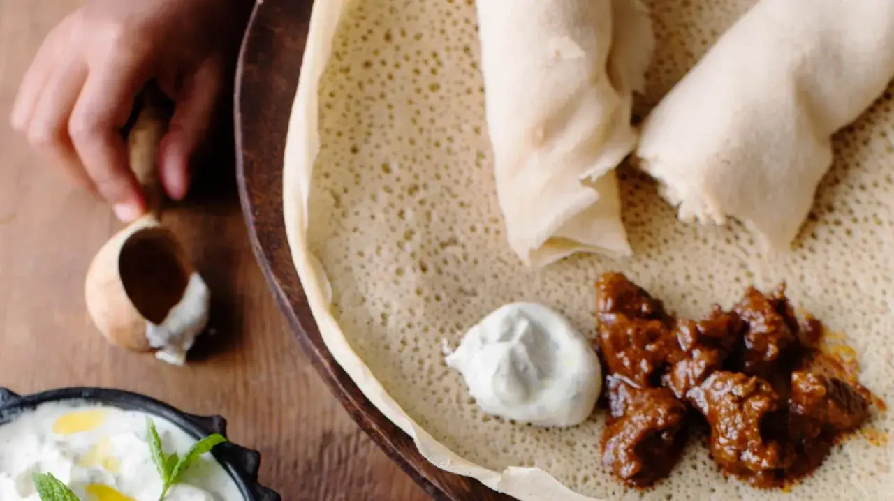 En hand tar en bit av injera, en etiopisk rätt med kött och sås. Ett enkelt injera recept att prova!