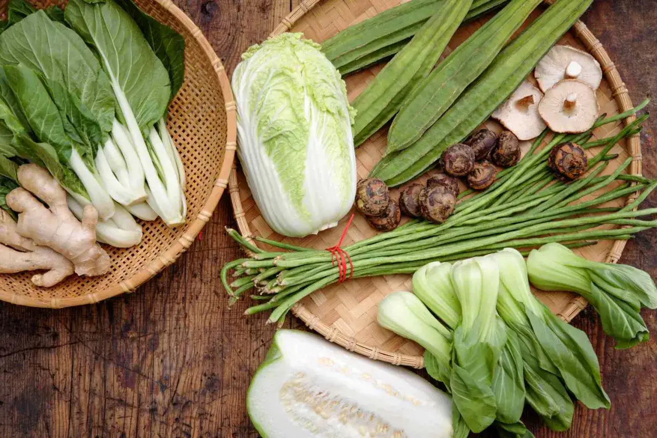 En korg med bok choy och ingefära bredvid en annan med kinakål, gurka, long beans och andra olika kålsorter.