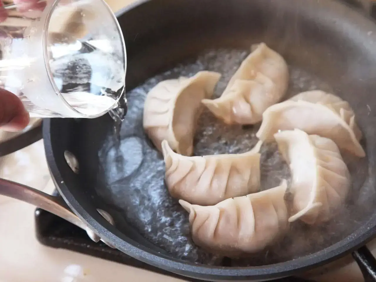 Vatten hälls i en stekpanna med dumplings, ett steg i ett enkelt dumplings recept.