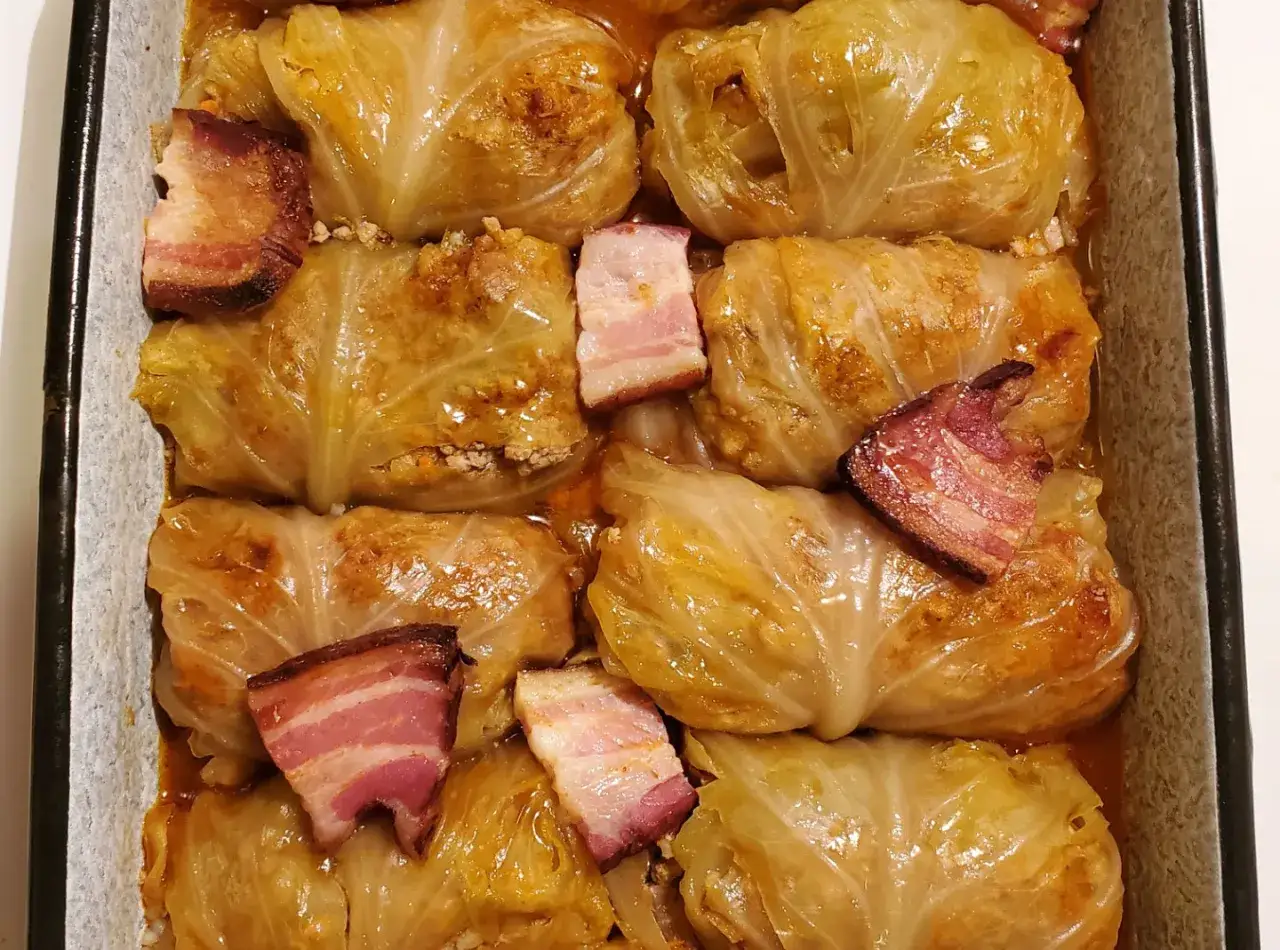 En ugnsform fylld med kåldolmar, ett klassiskt sarma recept, toppade med skivor av stekt bacon.