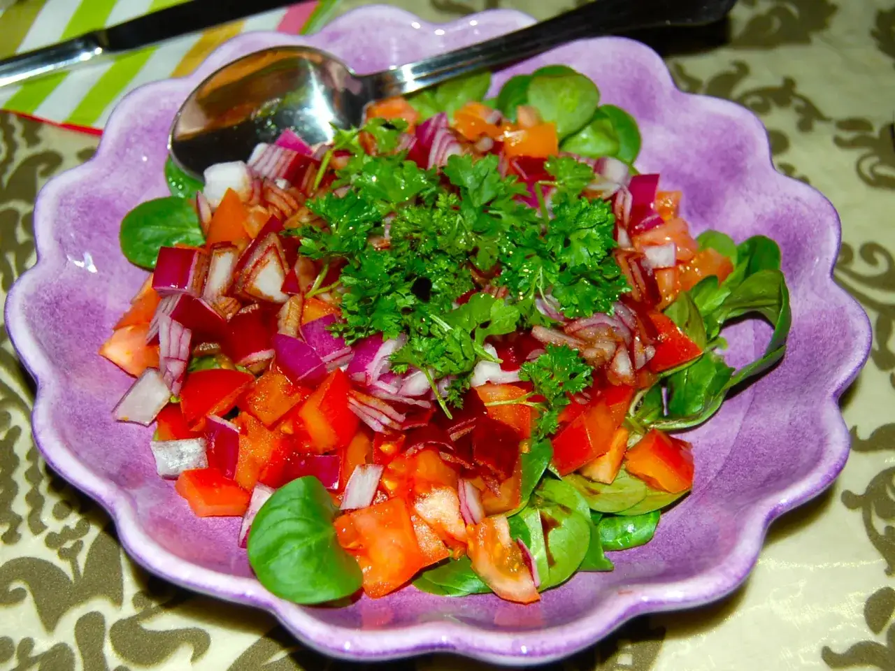 En färgglad sallad shirazi med tomater, rödlök och persilja i en lila skål.