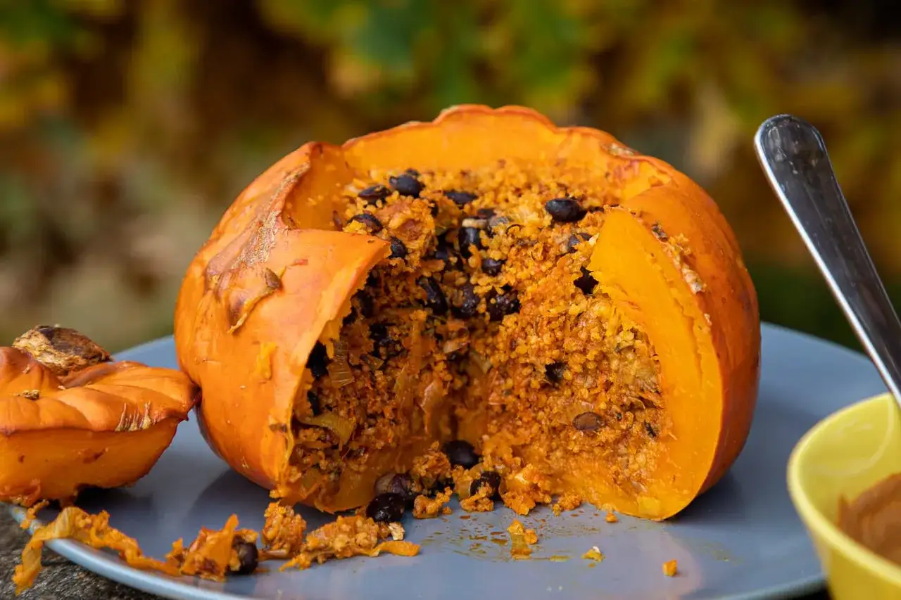 En hel pumpa hokkaido fylld med en smakrik blandning av couscous och svarta b&ouml;nor, redo att avnjutas.