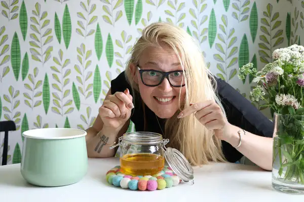 Glad kvinna visar upp sin hemgjorda ghee. Enkel guide för hur man gör ghee.
