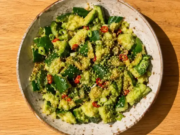 En skål med krossad gurka sallad, toppad med sesamfrön, chili och salladslök. En härlig och fräsch rätt.