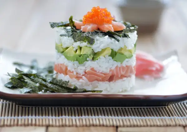 En vacker sushi tårta med lax, avokado och ris, toppad med rom och nori. En festlig rätt för alla sushiälskare.