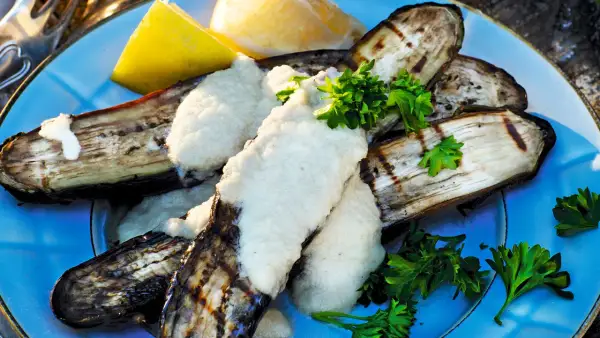 Grillad aubergine med en krämig sås och färsk persilja, serverad med citronklyftor. En härlig sommarrätt.